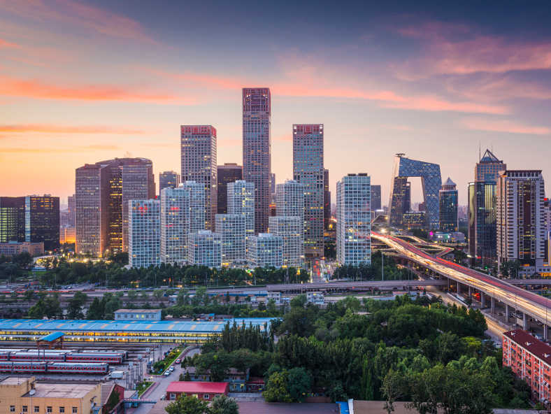 A panoramic view of a modern city skyline at dusk, featuring tall glass buildings and busy highways.