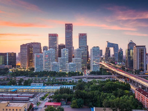 A panoramic view of a modern city skyline at dusk, featuring tall glass buildings and busy highways.